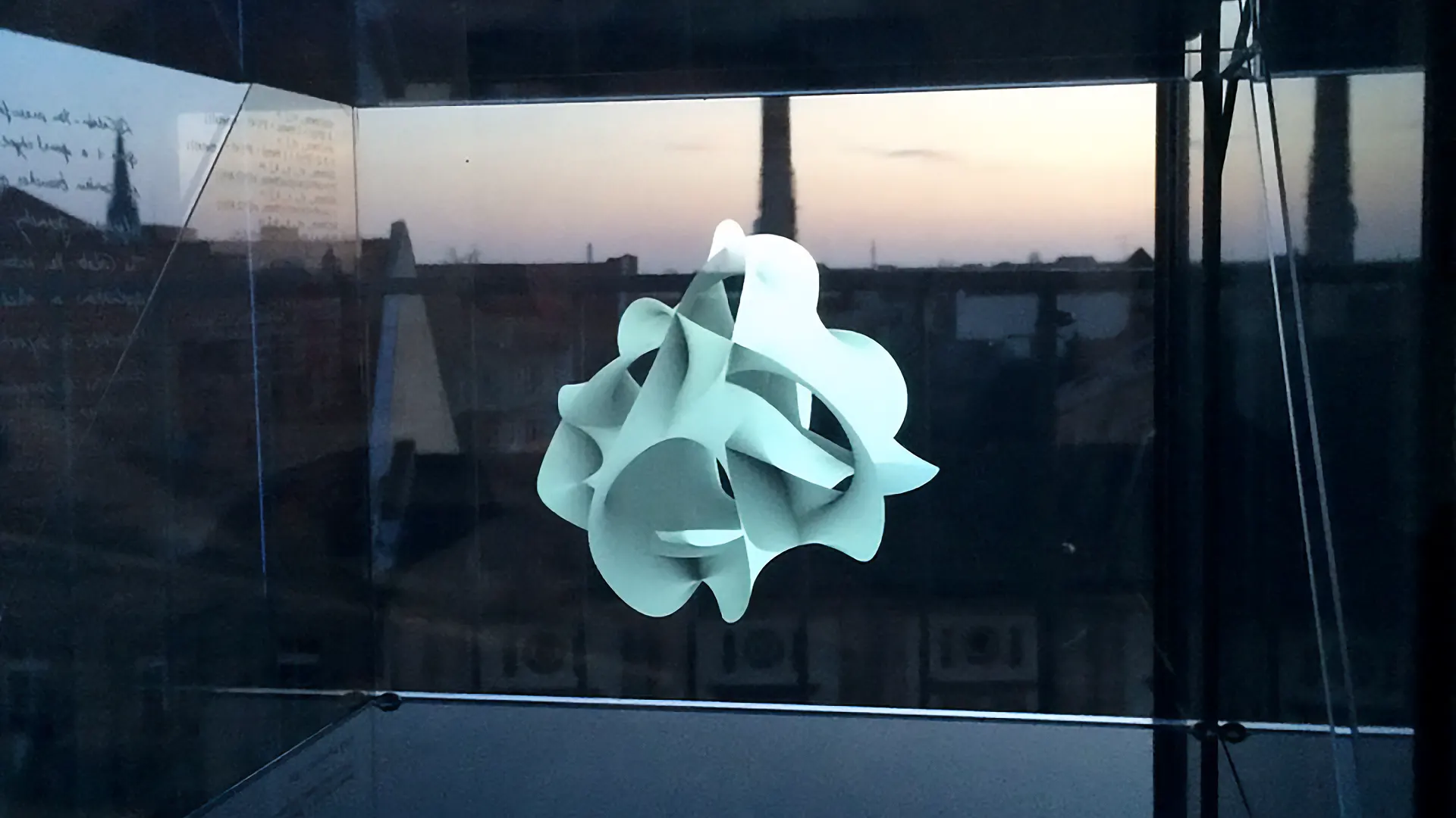A projected mathematical spherical shape inside a glass cube in front of the Berlin skyline.
