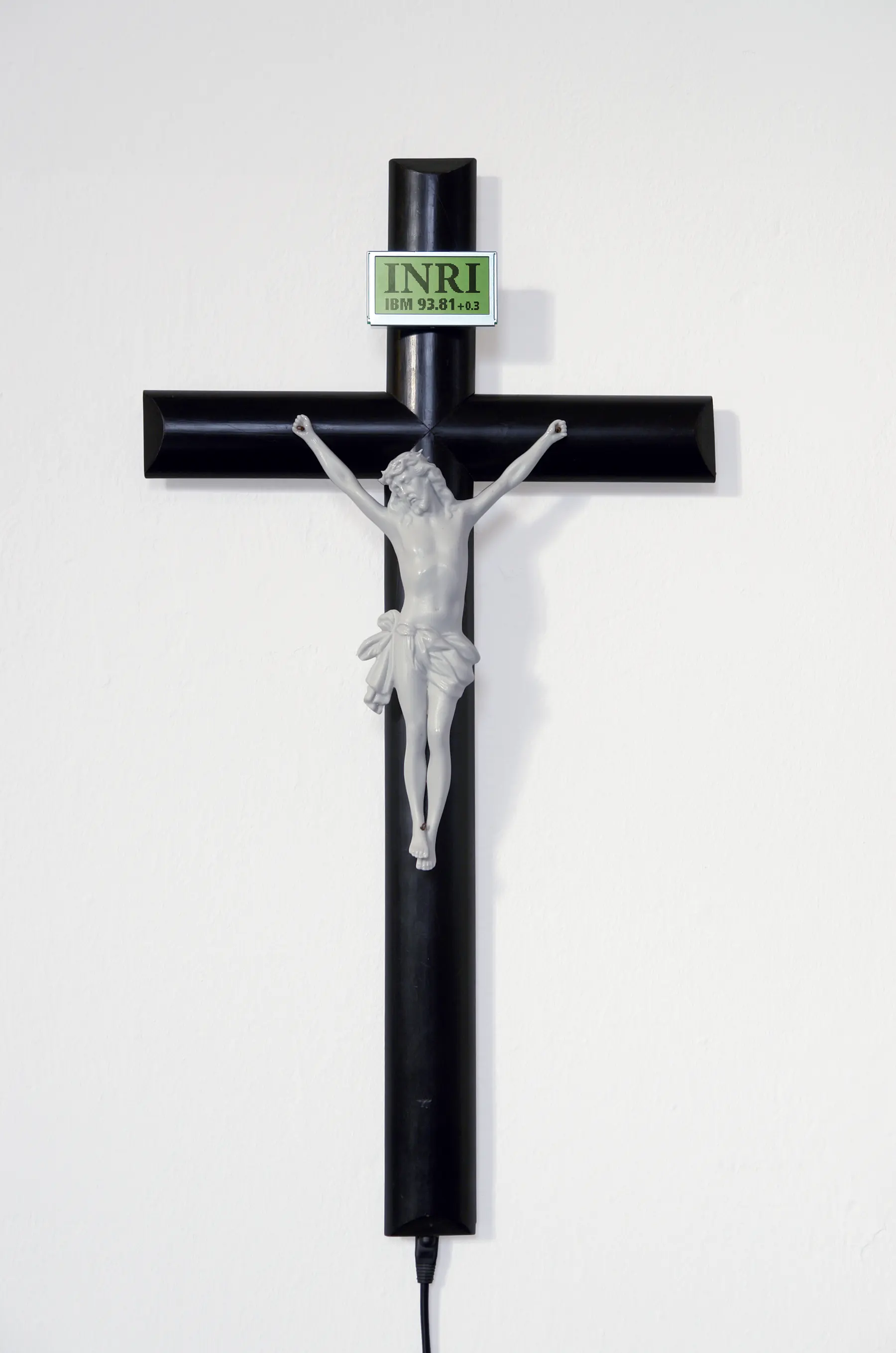 A crucifix. A the position of the INRI inscriptions sits a LCD screen, which displays stock excahnge prices: (IBM, Disney...)